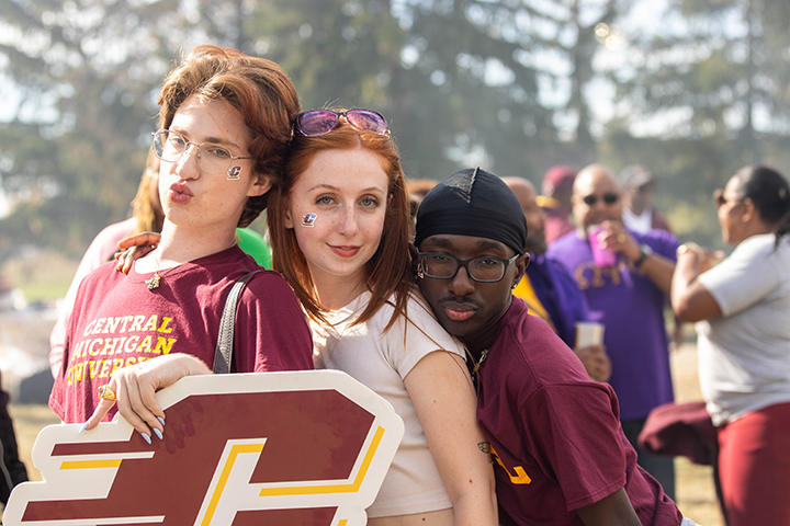 Three CMU students strike model poses for the camera while holding a large Action C sign.