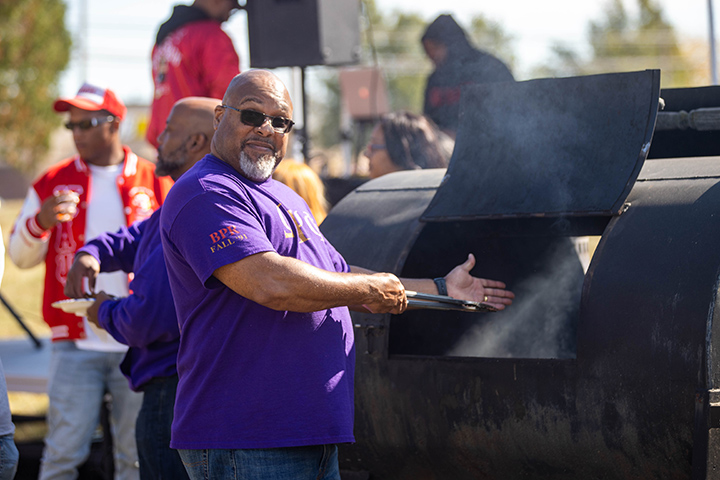 A man in a purple shirt shows off the inside of his large meat smoker.