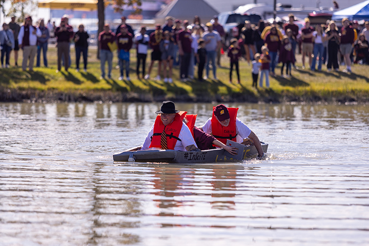 President Bob Davies wears a life vest and floats in a cardboard boat in Rose Pond.