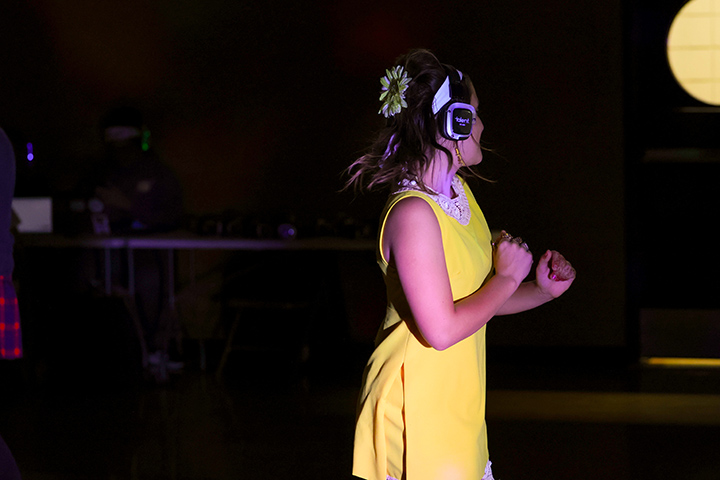 A student in a yellow dress dances while wearing headphones.