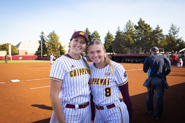 Two CMU softball players pose for a photo while standing neat the third baseline.