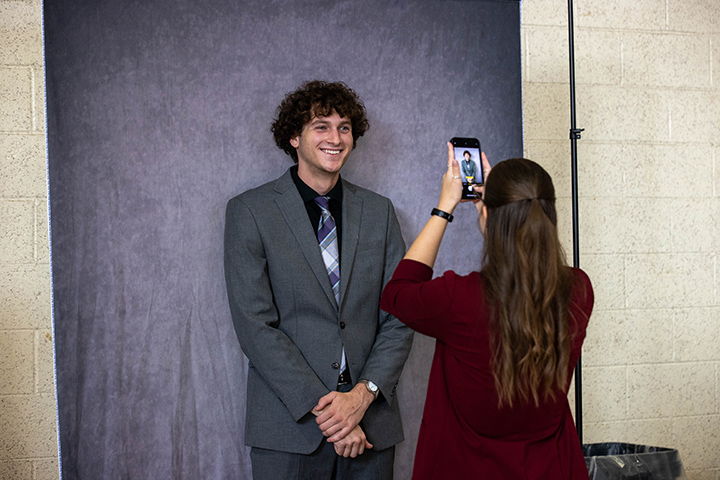 A student stands in front of a gray background while wearing a suit for a professional headshot.