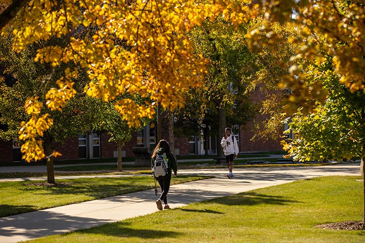 Two students walk down a sidewalk on CMU's campus surrounded by trees displaying fall colors.