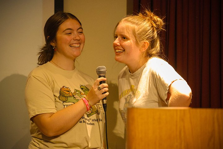 Two female college students perform karaoke while holding a microphone.