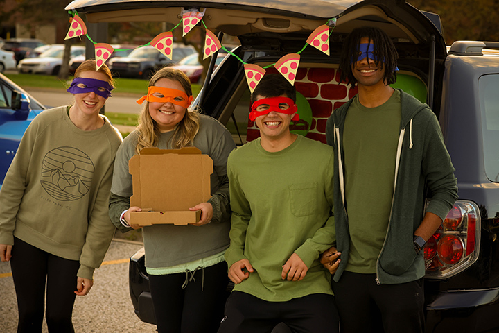 Four students dressed as Teenage Mutant Ninja Turtles hold a box of candy.