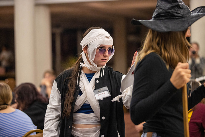 A student wearing sunglasses and dressed like a mummy stands next to another student dressed as a witch.