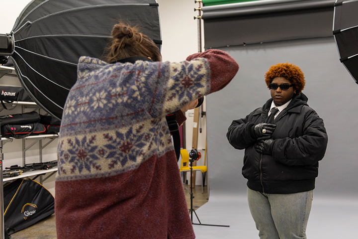 A photographer takes a person's photo in front of a gray paper backdrop.