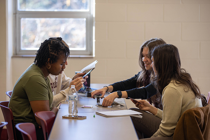 Four college students sit at a long table together playing a board game.