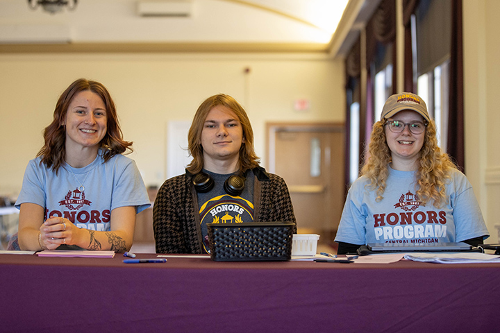 Three students smile for the camera while sitting at a table.