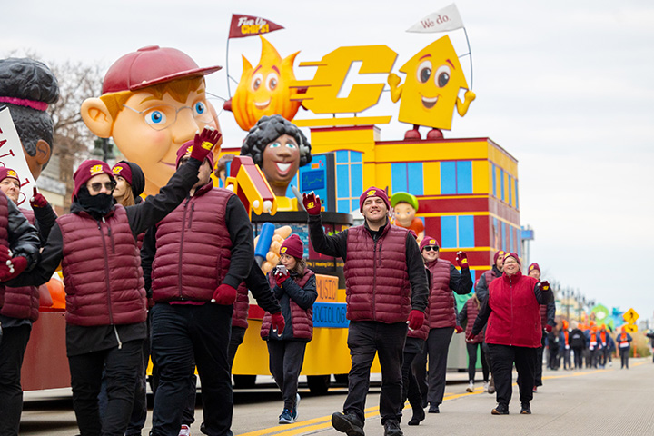 CMU volunteers walk and wave next to the CMU Thanksgiving parade float.