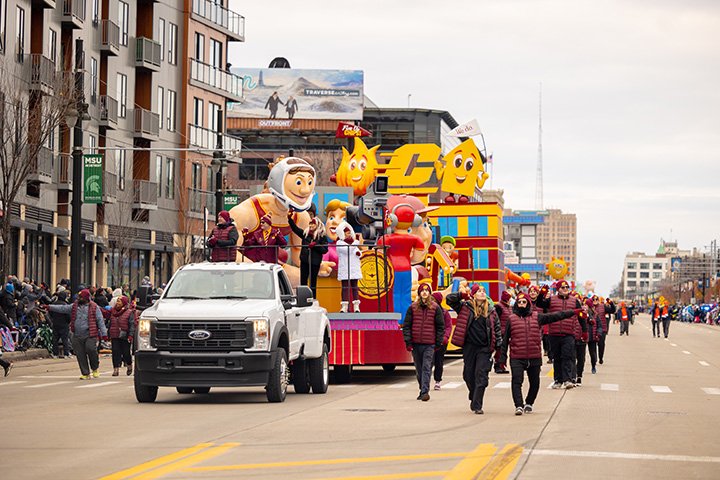 CMU volunteers walk and wave next to the CMU Thanksgiving parade float.