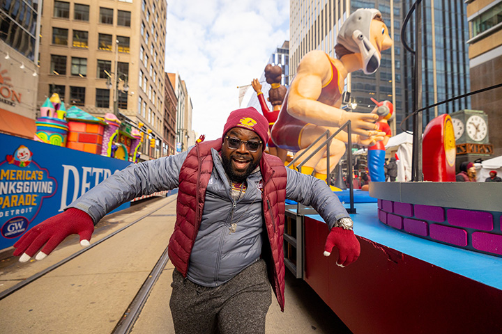 A parade volunteer runs towards the camera as the CMU parade float moves down the road in the background.