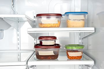 Five containers of leftover food sit on shelves in a refrigerator.