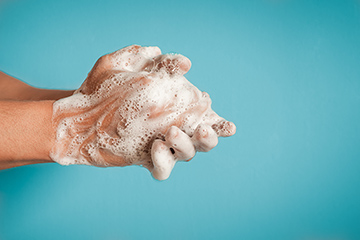 Two hands lathered in soap against a light blue background.