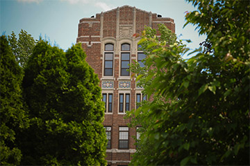 Lush green trees frame the main tower of CMU's administration building with clear blue skies in the background.