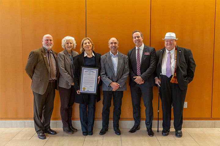 A group of men and women stand in front of a wooden wall holding a certificate