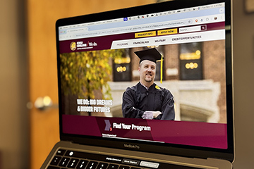 Photo of a laptop computer screen showing the CMU Online home page with a graduate in the middle of the page and the words Find Your Program underneath.