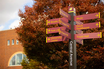 A set of maroon directional signs on a grey post that reads Central Avenue