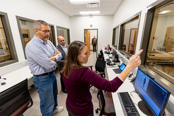 A woman points out health care equipment to two men in a screening room