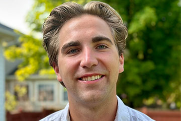 A close-up photo of man with blond upswept hair in a blue shirt.