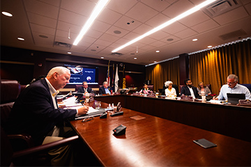 Board members sit around a large table covered with papers and laptop computers.