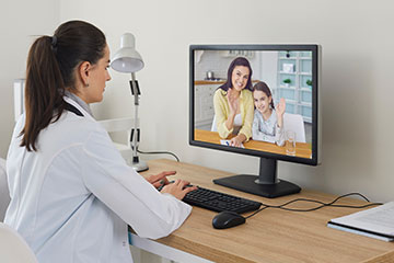 A doctor in a white coat looks at a computer screen showing a mother and child