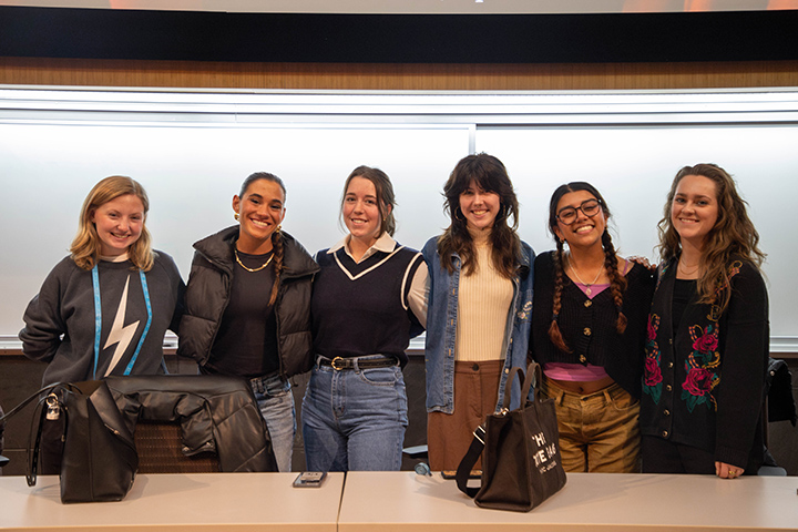 Six fashion design students stand for a group photo in a classroom.