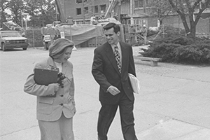 Black and white photo of Betty Wagner holding a clipboard and walking on campus alongside CMU's 12th president Michael Rao.