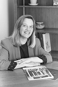 Black and white photo of Betty Wagner sitting at a desk with CMU brochures laid out in front of her and smiling in 1998.