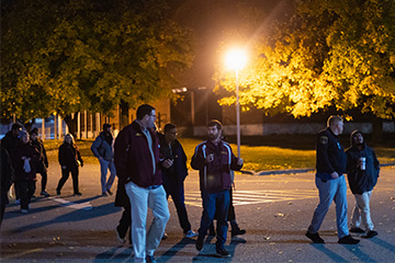 A group of people walking in a parking lot at night.