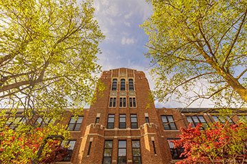 Warriner Hall, a multistory red brick building with many windows, appears surrounded by green trees and pink flowers.