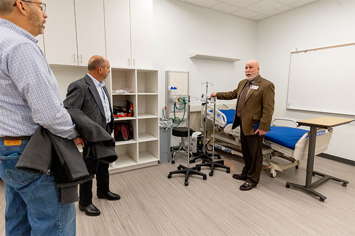 Three men stand in a healthcare simulation room.