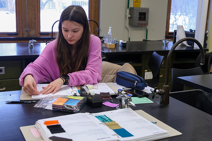 A student sits at a desk as three-ring binders sit open.