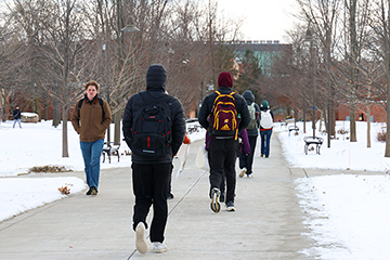 Students walk down a sidewalk surrounded by snow.