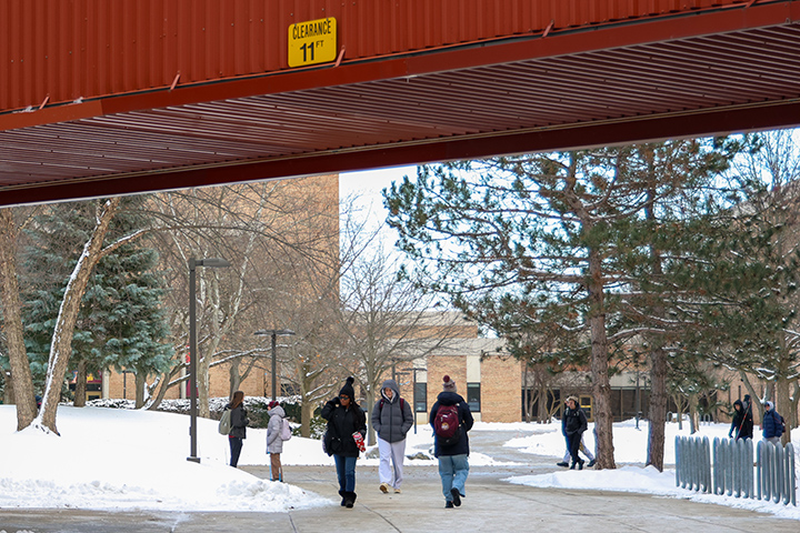 Students want down a sidewalk that goes underneath an enclosed walkway.