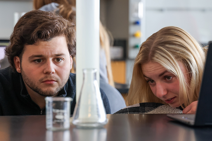 A closeup of two students' heads as they look at chemistry equipment on a table.