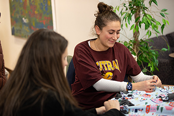 Two female students sit at a table making a mitzvah.