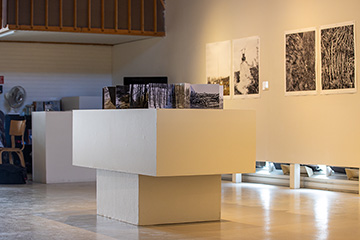 Inside the University Art Gallery, a white t-shaped table stands with art on top of it.