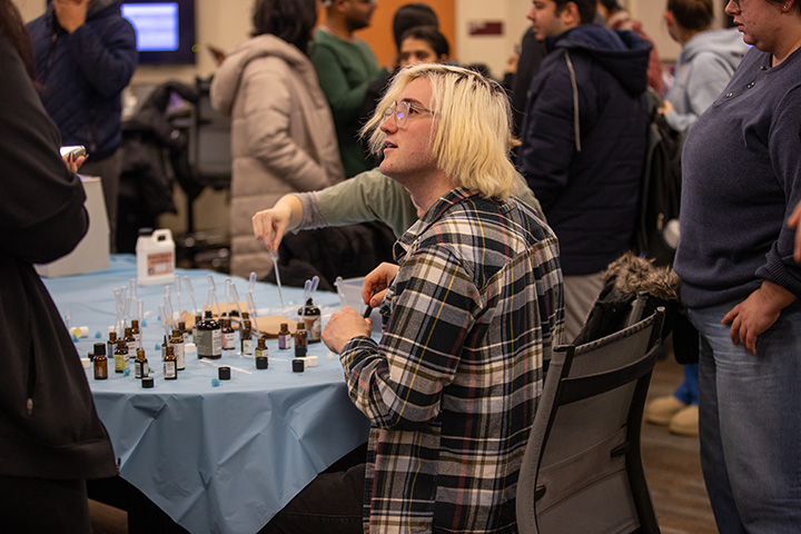 A blond student sits at a table creating perfumes in small bottles.