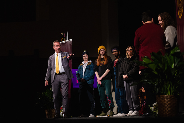 President MacKinnon stands on stage next to 10 people.