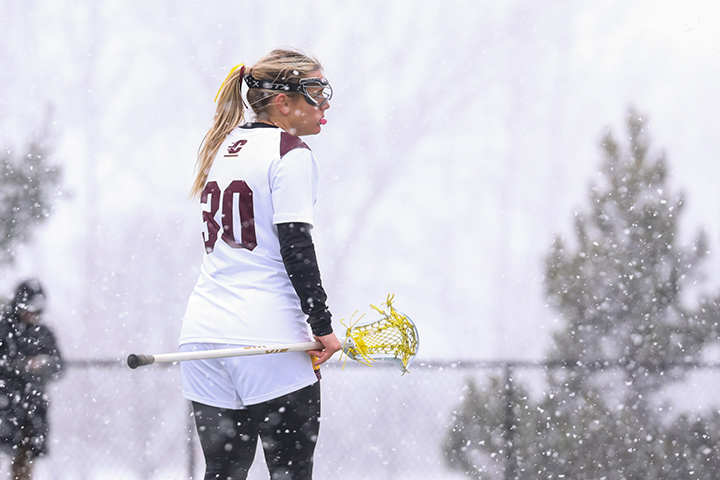 A women's lacrosse player stands on a snowy field holding her stick.