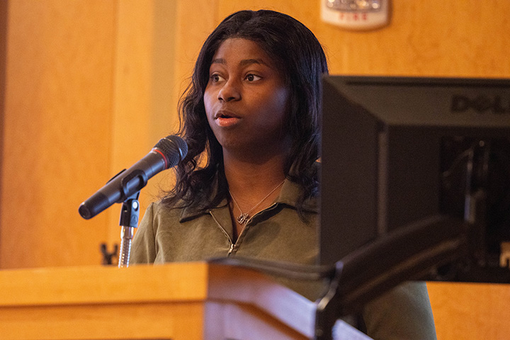 A college student stands at a podium speaking into a microphone.