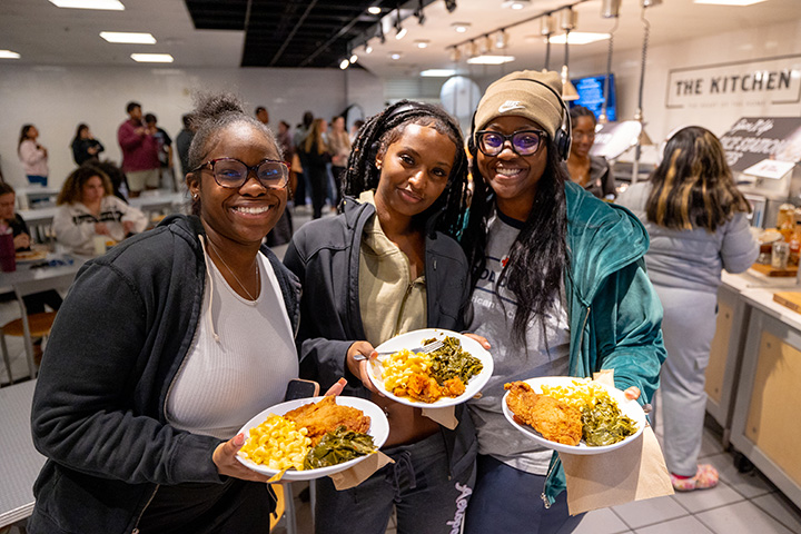 Three college students hold plates of food at a Black History Month dinner.