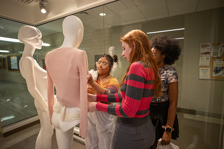 Three fashion design students dress mannequins.