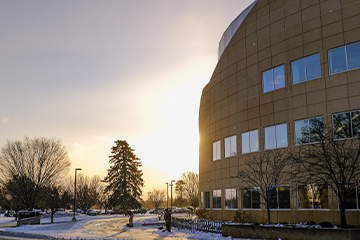 An academic building with snow and trees.