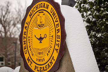 The maroon and gold seal of CMU with a dusting of snow on it.