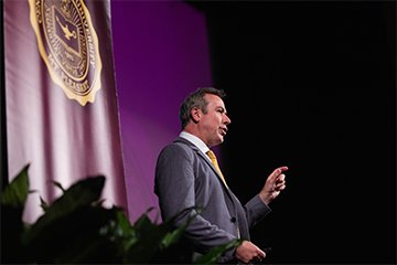 A man standing standing on a stage delivering a speech.