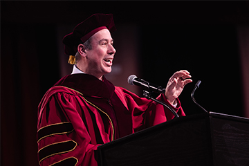 A man in a red robe speaking into a microphone.