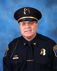 A police officer in uniform sits in front of a blue background