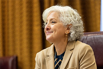 A close-up image of a smiling woman in a gold blazer